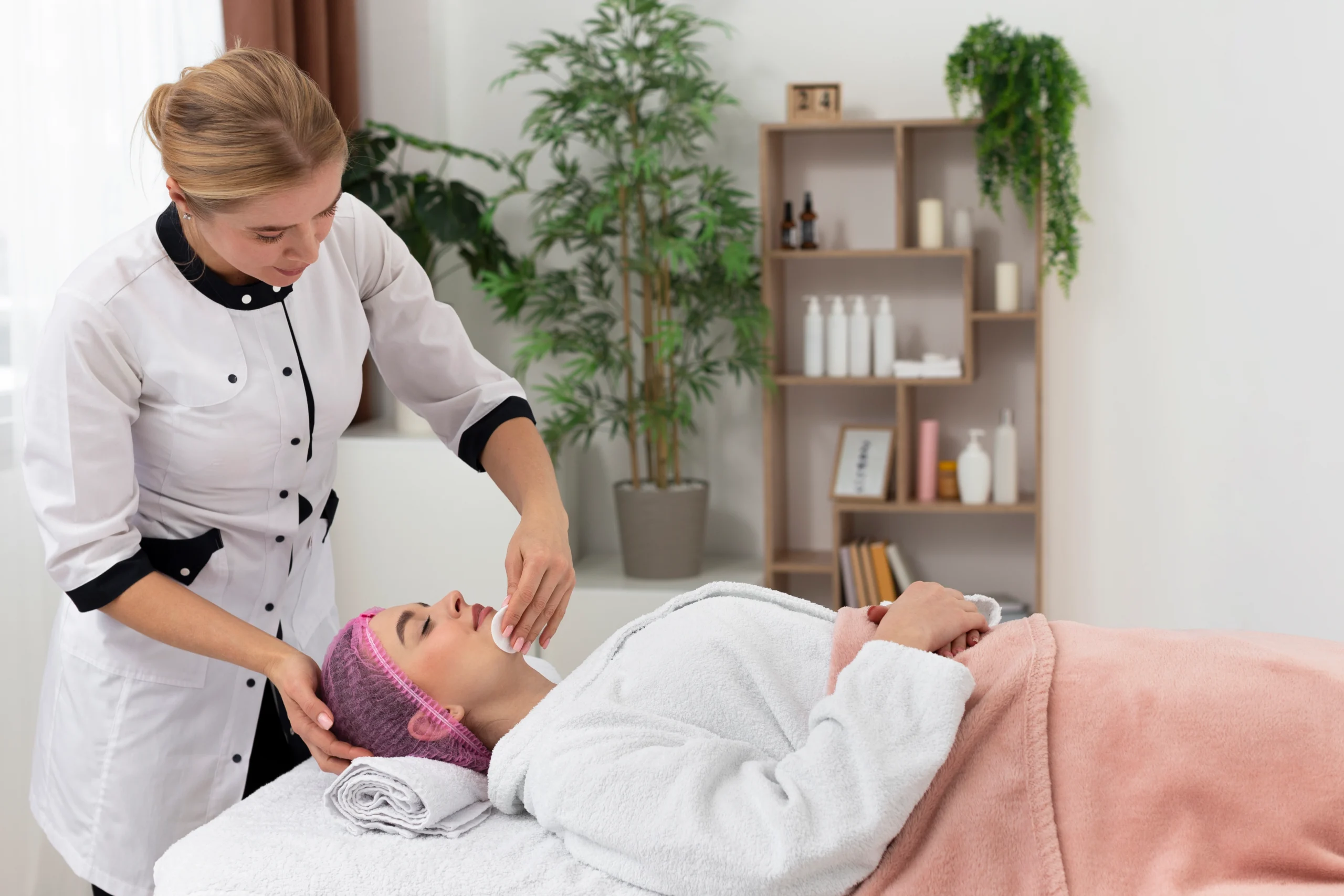 Professional beautician performing a facial treatment for a woman lying on a spa bed, offering salon at home services in Ghaziabad with a clean and relaxing setup.